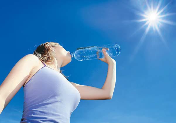 Mulher tomando água e se hidratando no verão